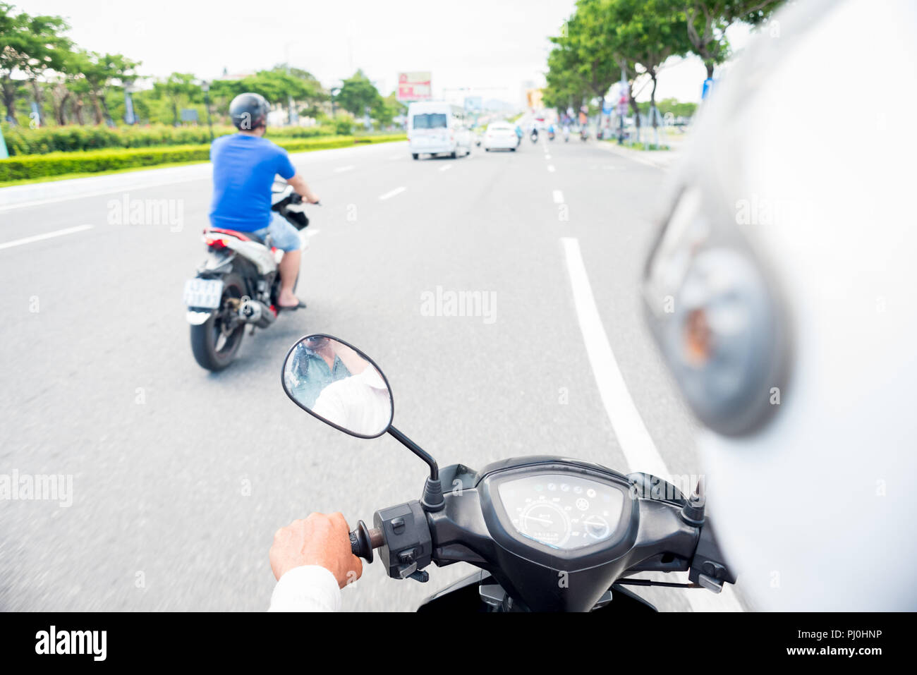 Vista da dietro il motociclo schiena del pilota. Casco bianco, moto di dashboard & la strada con uno scooter proseguendo verso altri tipi di traffico Foto Stock