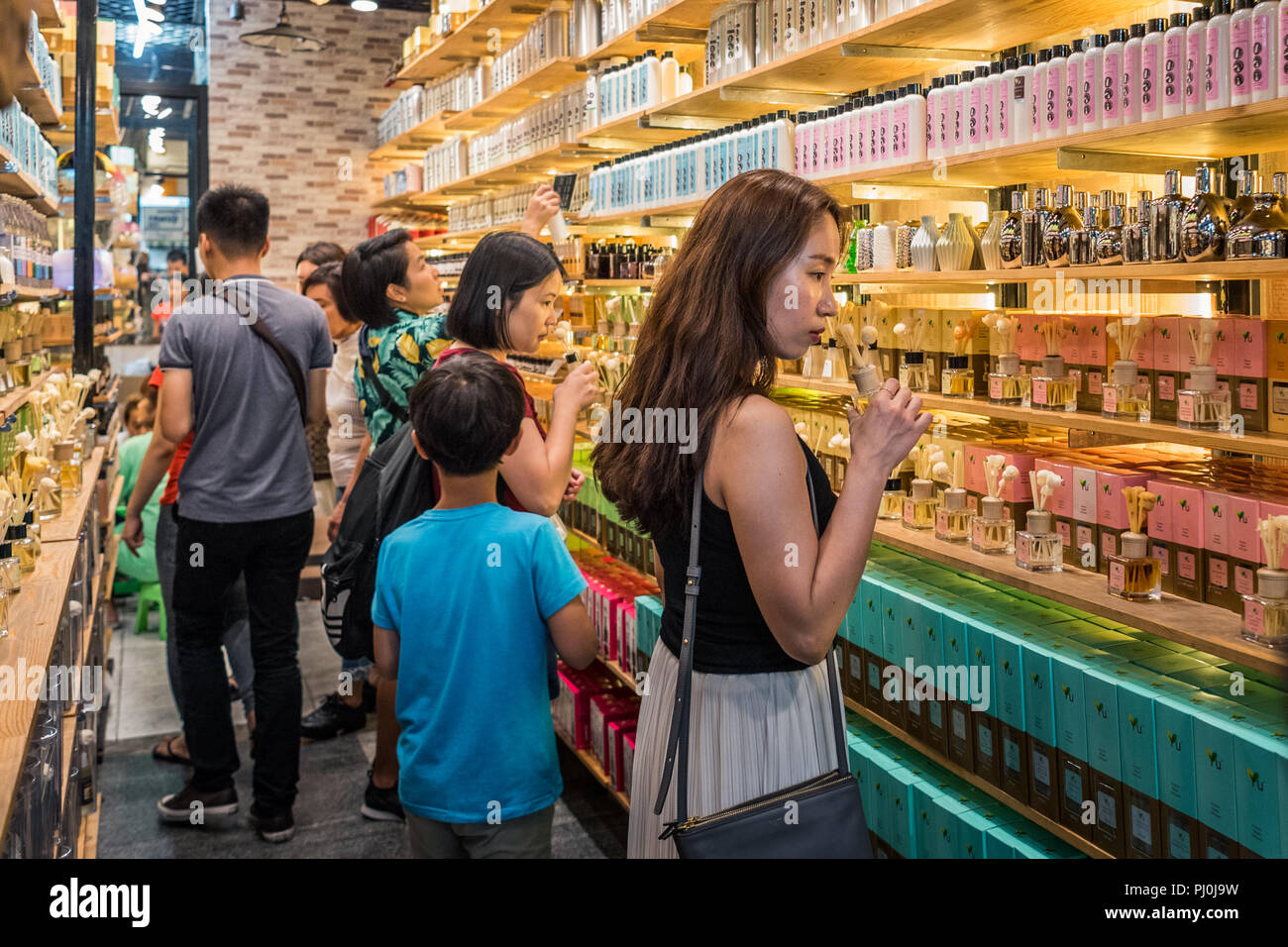 Le donne di odore oli profumati in piedi lungo mensole riempito con file di bottiglie con aromi in un negozio di odori al mercato di Chatuchak, Bangkok Foto Stock