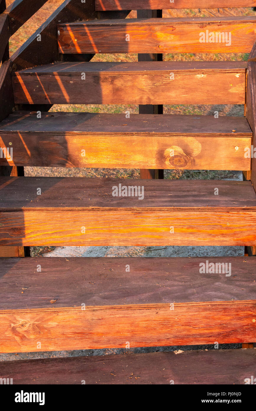 Una vista ravvicinata del sole splendente su una rampa di scale in legno che conduce al livello successivo di un edificio esterno Foto Stock