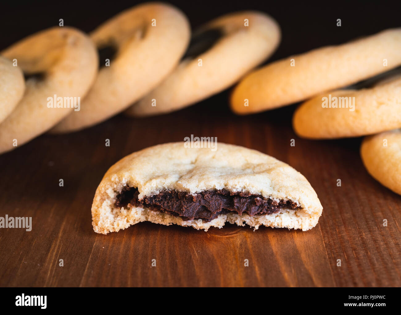 Cioccolata ripiena cookies tagliato a metà con crema di cioccolato e biscotti nel retro su sfondo di legno Foto Stock
