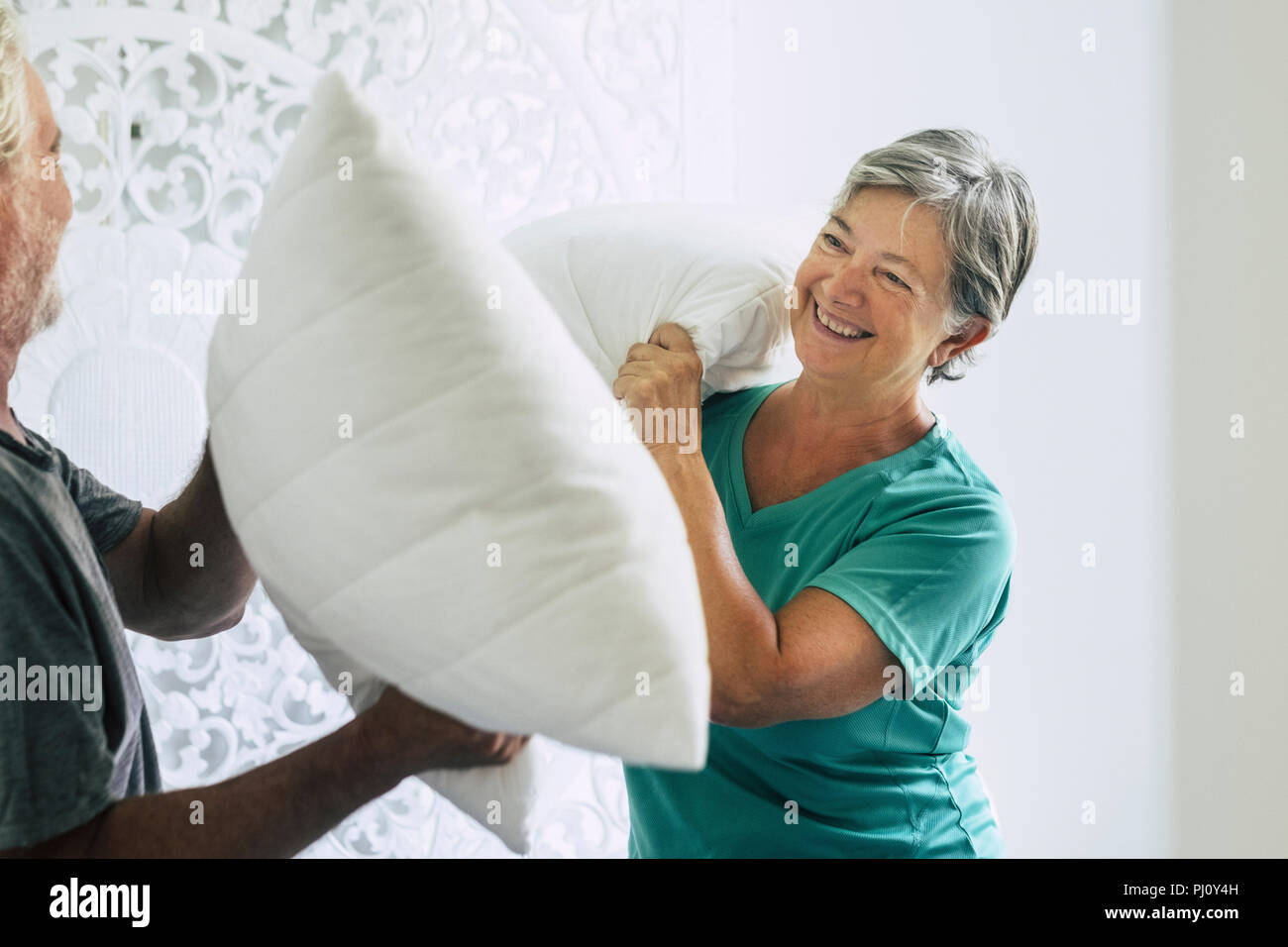 Cuscini guerra in casa per la caucasian paio di giocoso senior adulto uomo e donna giocare in camera da letto al mattino. felicità e gioia insieme per sempre s Foto Stock
