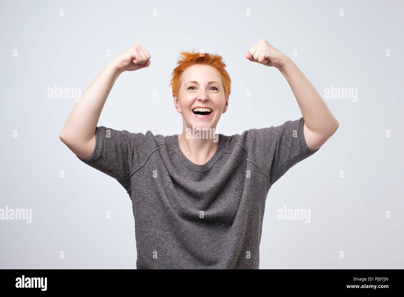 Allegra donna matura sorridente con pugni in rilievo che mostra la sua forza e la sua atmosfera positiva. Foto Stock