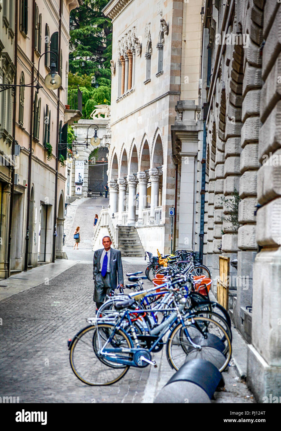 Uomo in tuta balade strada appena fuori la Plazza della Liberta, vicino alla Loggia del Lionello con biciclette parcheggiate in edili a Udine, Italia Foto Stock