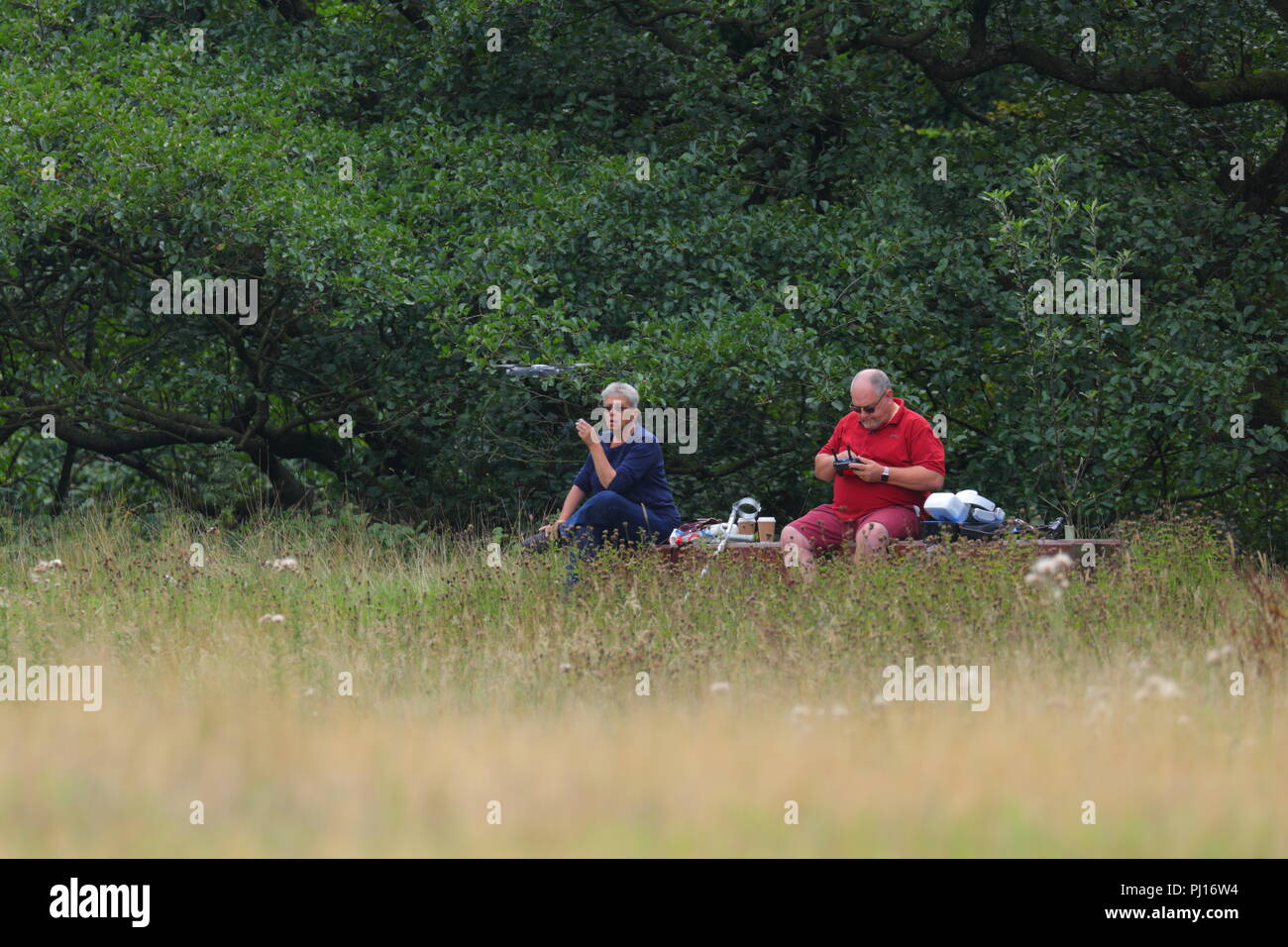 Un uomo e una donna seduti su una panchina mentre l'uomo mosca un drone in Peak District. Foto Stock