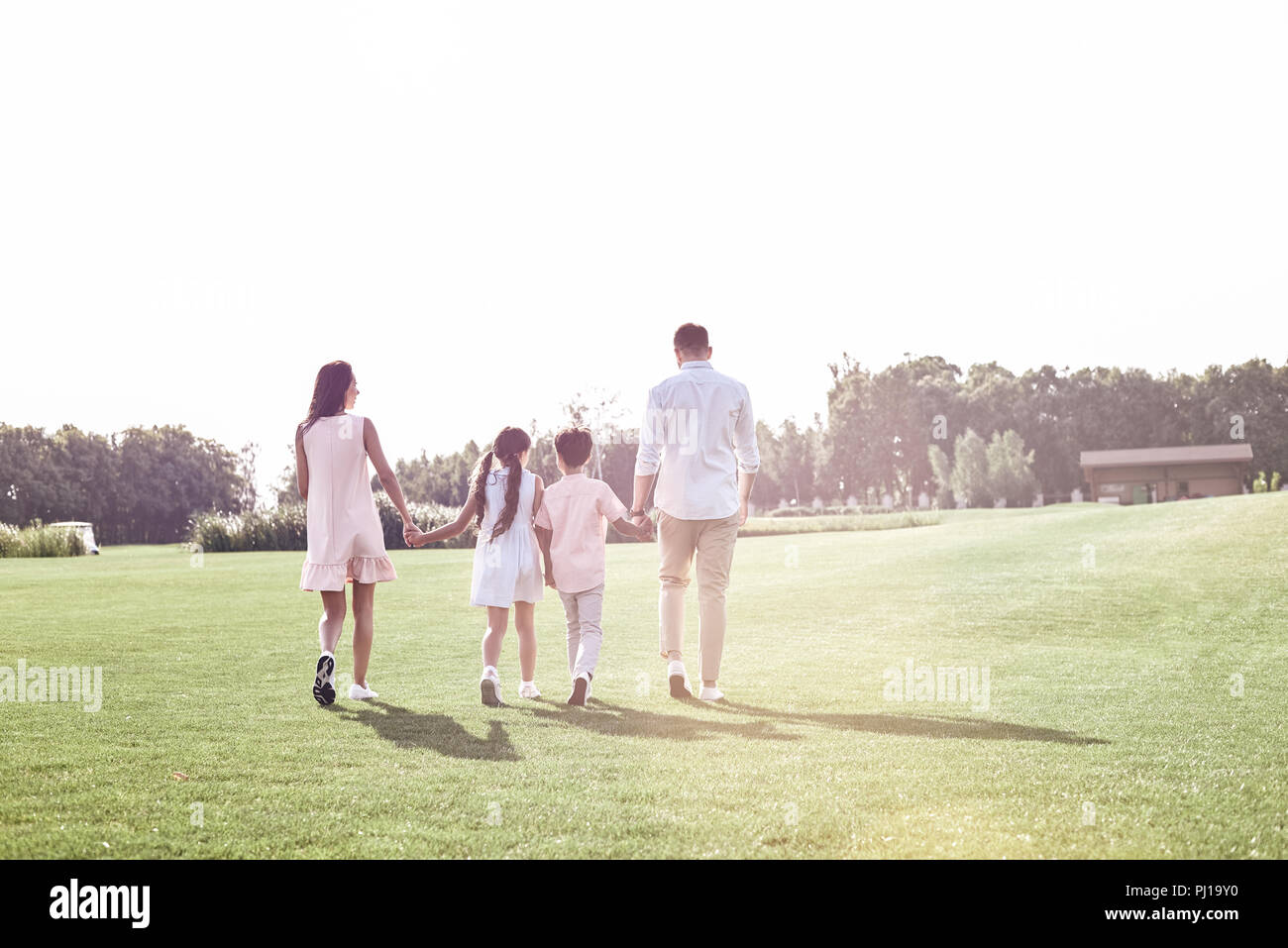 L'incollaggio. Famiglia di quattro camminando sul campo erboso vista posteriore Foto Stock