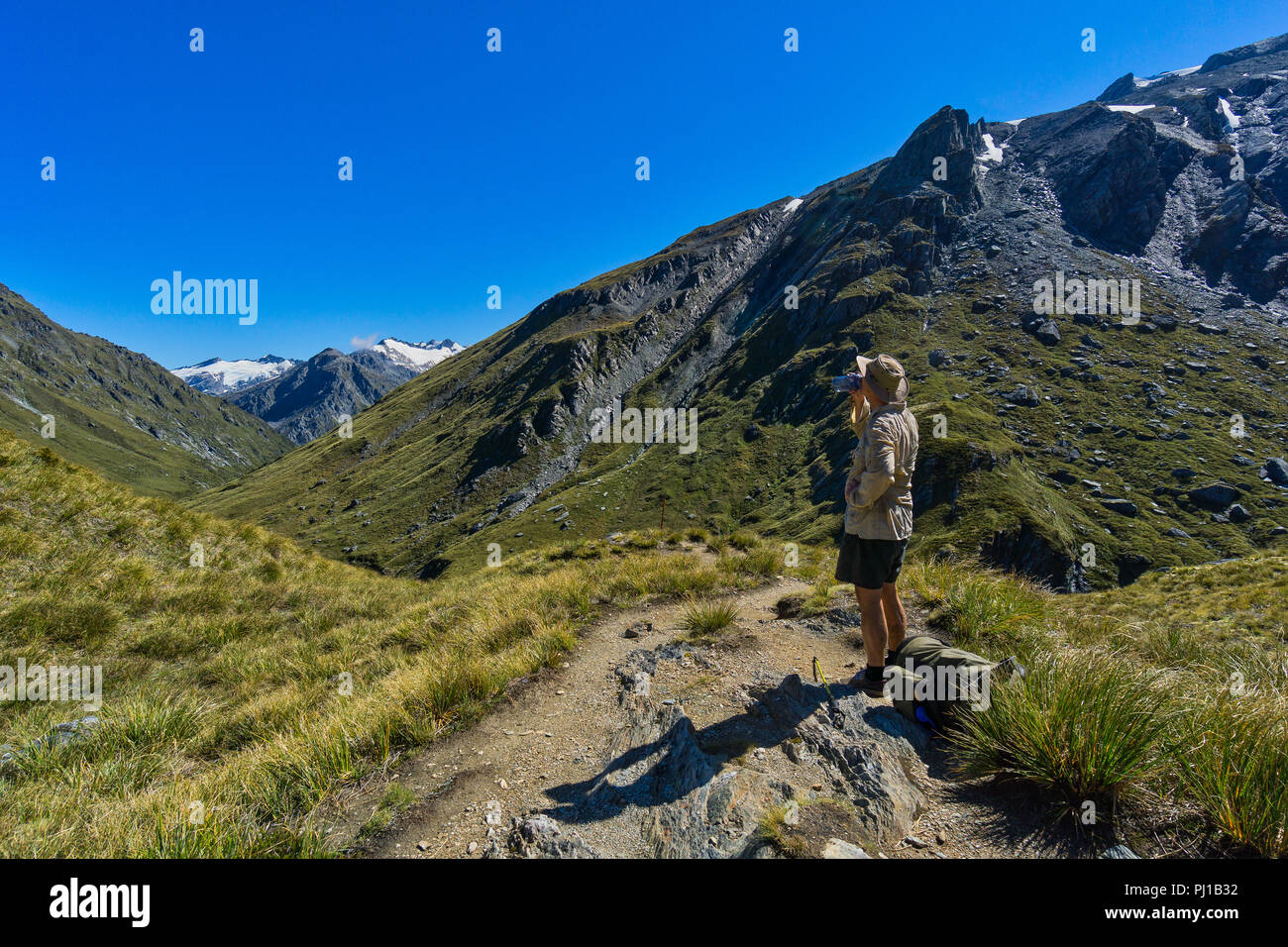 Escursionista prendendo una pausa di acqua, Rees sella, Rees-Dart via, Mt Aspiring National Park, Isola del Sud, Nuova Zelanda Foto Stock
