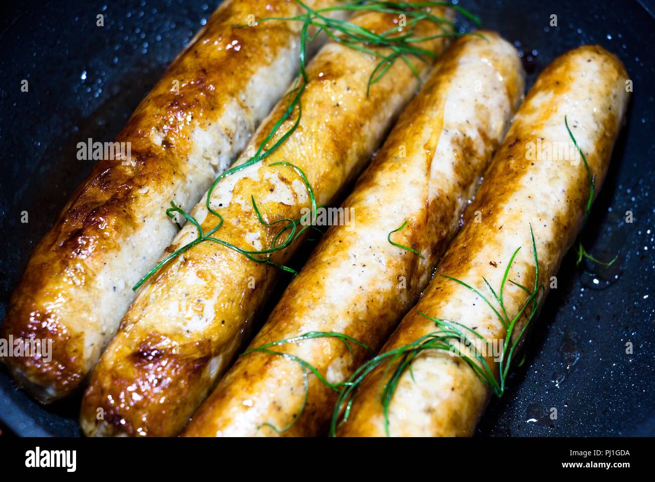 A pochi fritti, freschi e fragranti salsicce, giacciono su un nero padella e friggere. Sono decorate con freschi e aneto utili. Molto gustoso cibo da natur Foto Stock