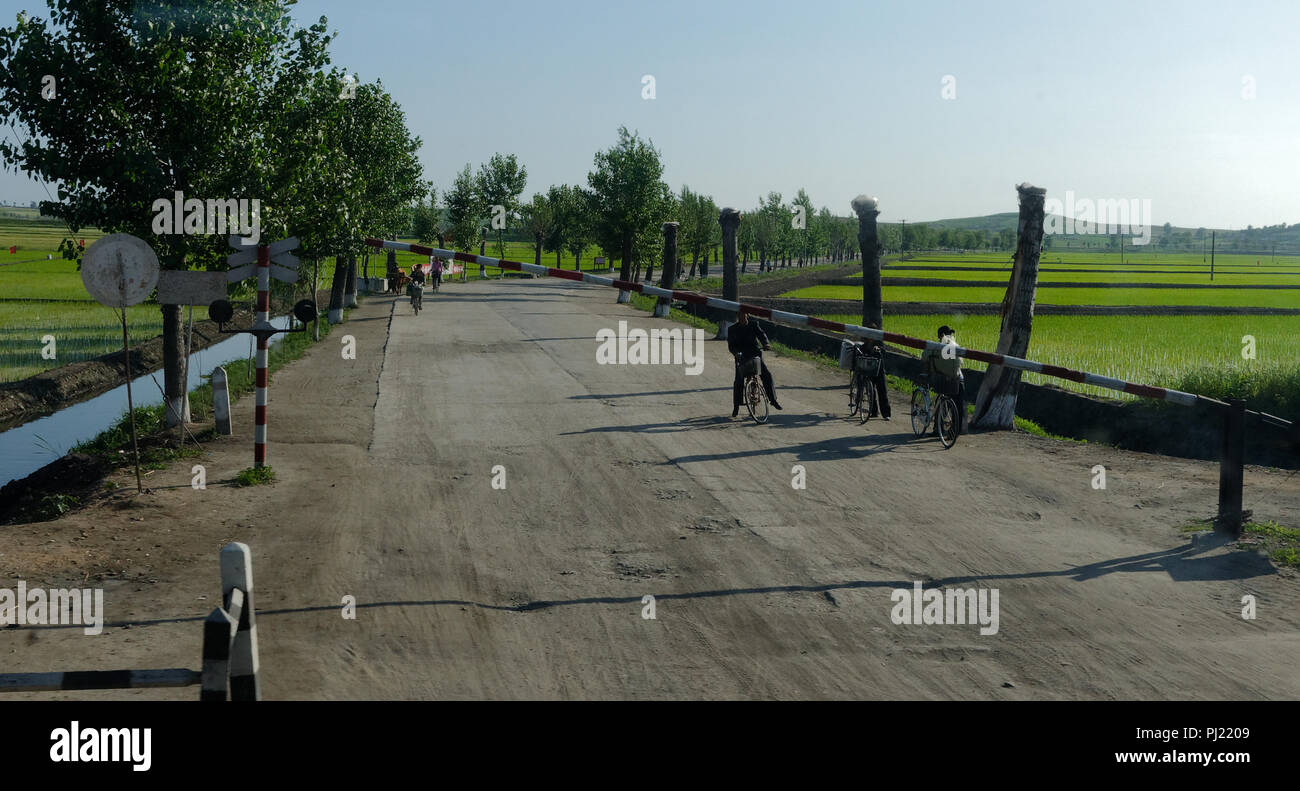 I pedoni e i piloti del ciclo di fermarsi in corrispondenza di una barriera manuale su un attraversamento ferroviario, Corea del Nord Foto Stock