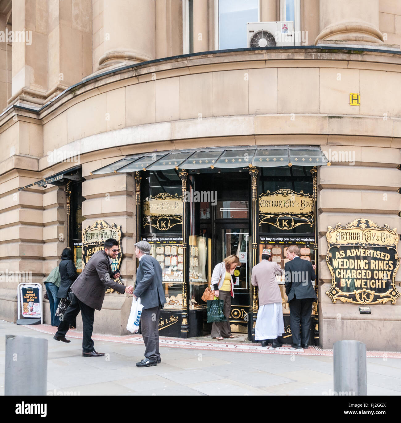 Due uomini di diverse età e le gare di conversazione e di salutare ciascuno di altri al di fuori di Arthur Kay gioiellerie in Manchester Foto Stock