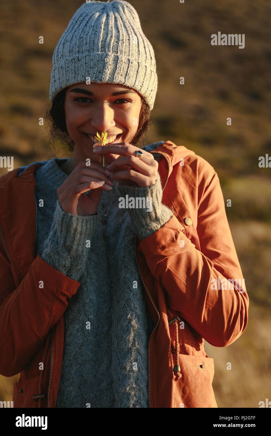 Ritratto di carino giovane donna in inverno indossare odorare un fiore. Femmina in vestiti caldi permanente sulla montagna e sorridente con un fiore in mano. Foto Stock