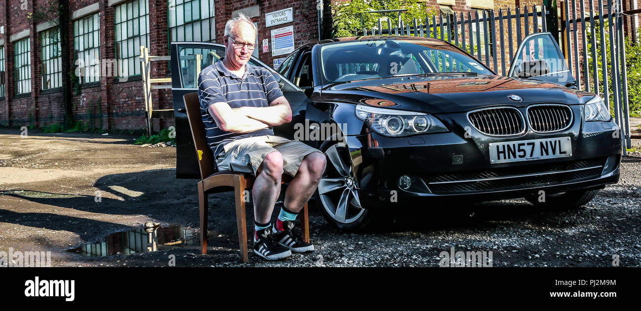 Uomo di mezza età seduto su una sedia accanto alla sua BMW Serie 5 berlina Foto Stock