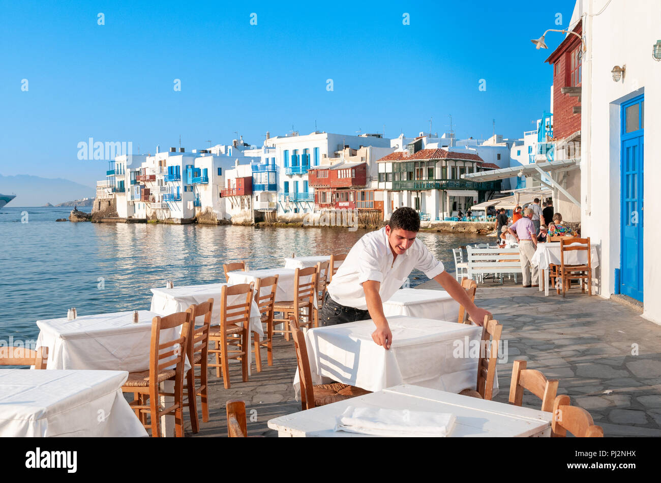 Cameriere che stabilisce le tabelle a waterfront restaurant in Little Venice, Mykonos, Grecia Foto Stock