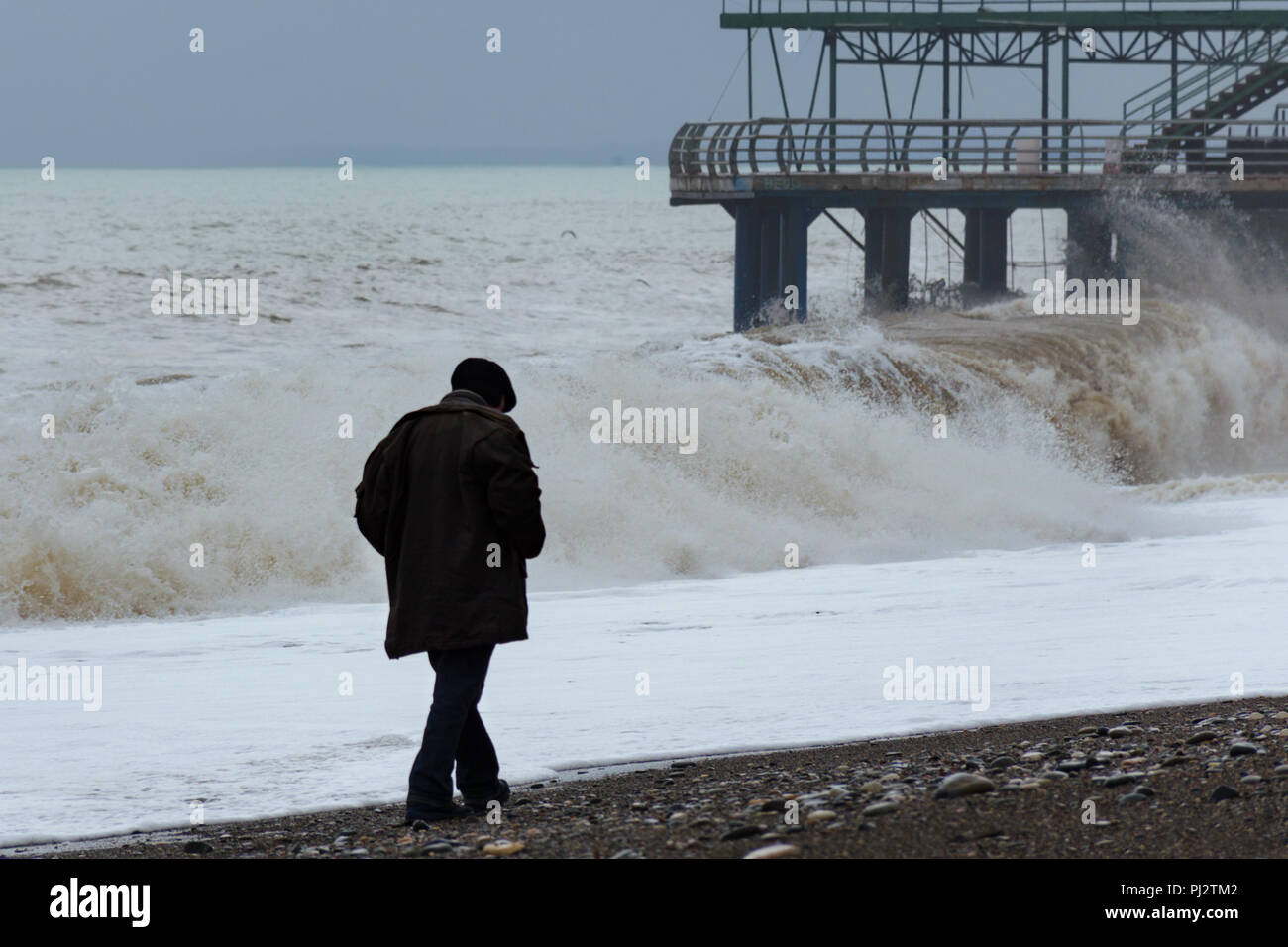 Drammatico, tempeste, mare spiaggia con grandi onde, singolo, lonely vecchio uomo a camminare lungo la costa, vista posteriore. Concetto di solitudine, anima-la ricerca. Foto Stock