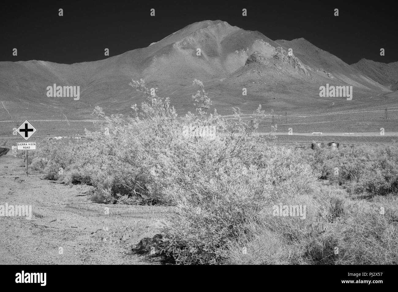 Autostrada segno e la spazzola nel deserto con alte montagne brulle sotto un cielo nero. Foto Stock