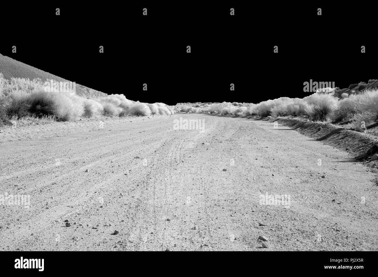 Una solitaria lungo strade sterrate corre nel deserto sotto una luce cielo nero. Foto Stock