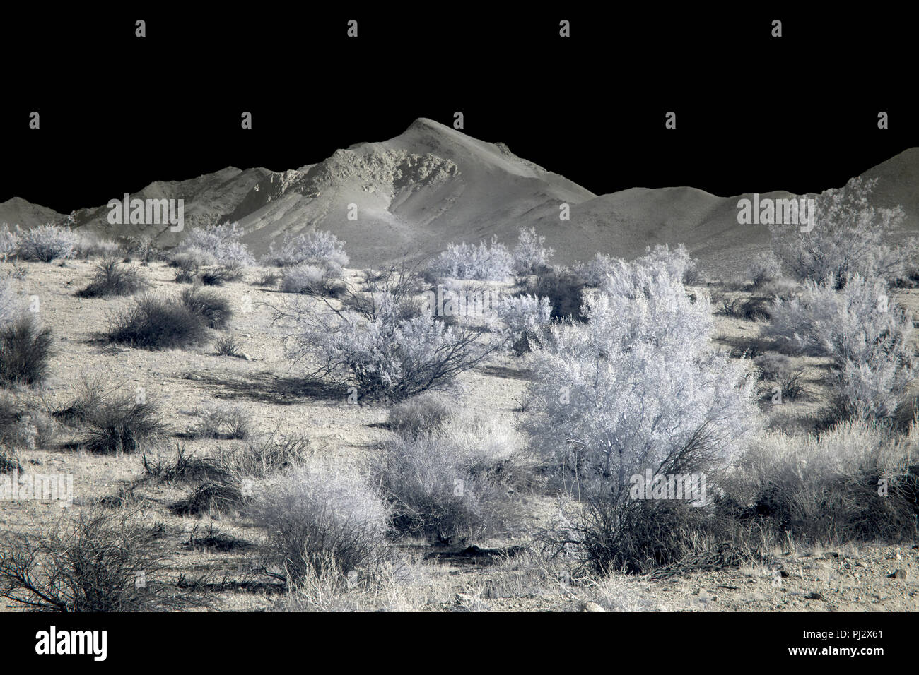 Vallata desertica con montagne sotto un cielo nero. Foto Stock