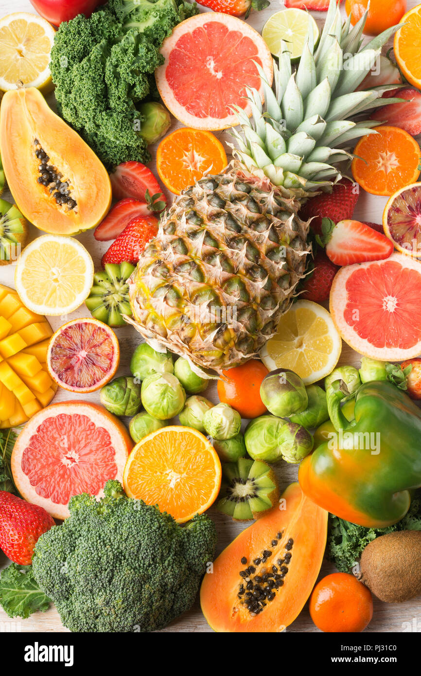 Frutta e verdura ricca di vitamina C la configurazione di sfondo, Arance Pompelmi mango kiwi Kale pepe al limone Ananas Papaia cavoli broccoli, verticale, sul tavolo bianco, vista dall'alto, il fuoco selettivo Foto Stock