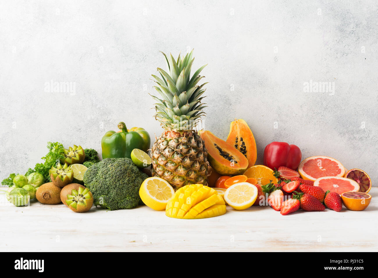 Colorata frutta e verdura ricca di vitamina C nei colori dell'arcobaleno, Arance Pompelmi mango kiwi Kale pepe al limone Ananas Papaia broccoli, sul tavolo bianco, copiare lo spazio per testo, il fuoco selettivo Foto Stock
