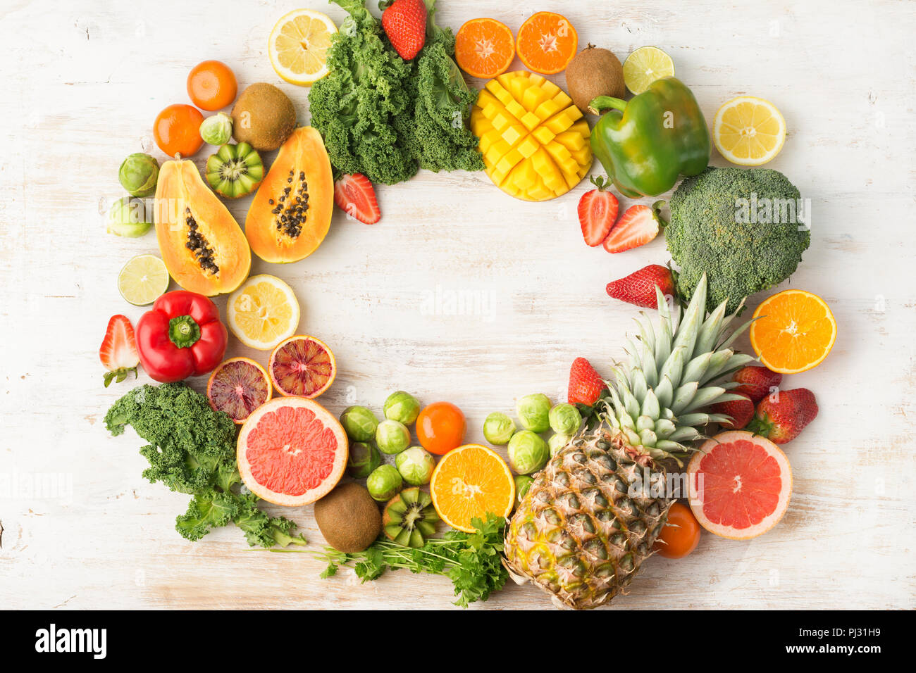 Frutta e verdura ricca di vitamina C in un telaio, Arance Pompelmi mango kiwi Kale pepe al limone Ananas Papaia cavoli broccoli, su legno tavolo bianco, vista dall'alto, copia di spazio, il fuoco selettivo Foto Stock