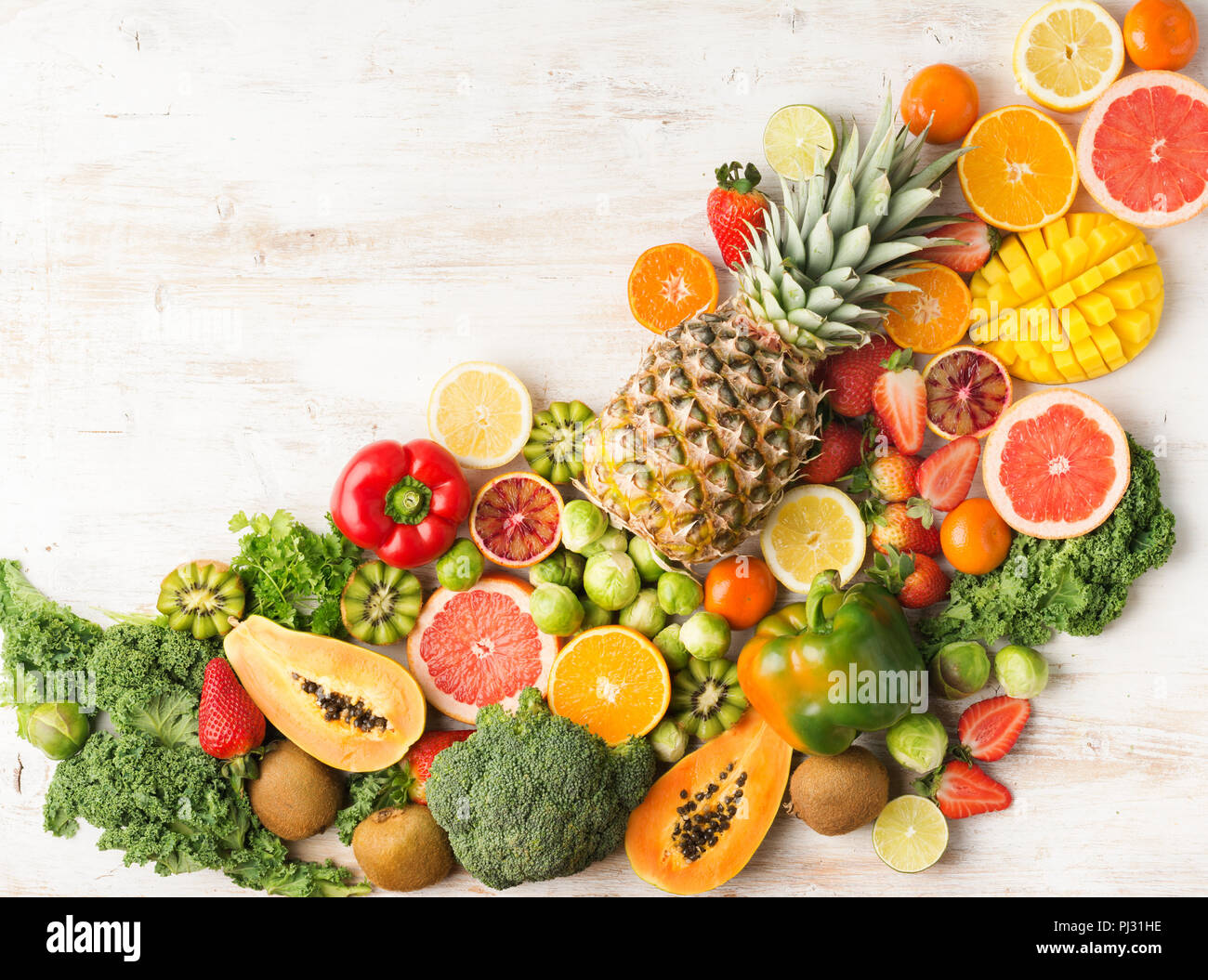 Frutta e verdura ricca di vitamina C disposte diagonalmente Arance Pompelmi mango kiwi Kale pepe al limone Ananas Papaia cavoli broccoli, sul tavolo bianco, vista dall'alto, copia di spazio, il fuoco selettivo Foto Stock