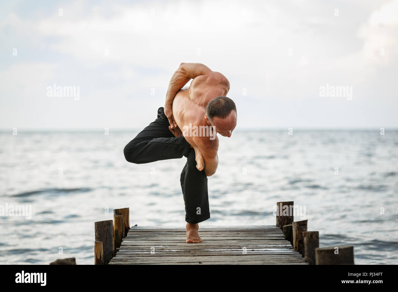 Giovani trainer di yoga pratica di esercizi yoga su un molo in legno su un mare o riva del fiume. Uno stile di vita sano concetto Foto Stock