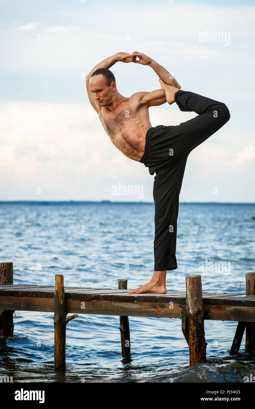 Giovani trainer di yoga pratica di esercizi yoga su un molo in legno su un mare o riva del fiume. Uno stile di vita sano concetto Foto Stock