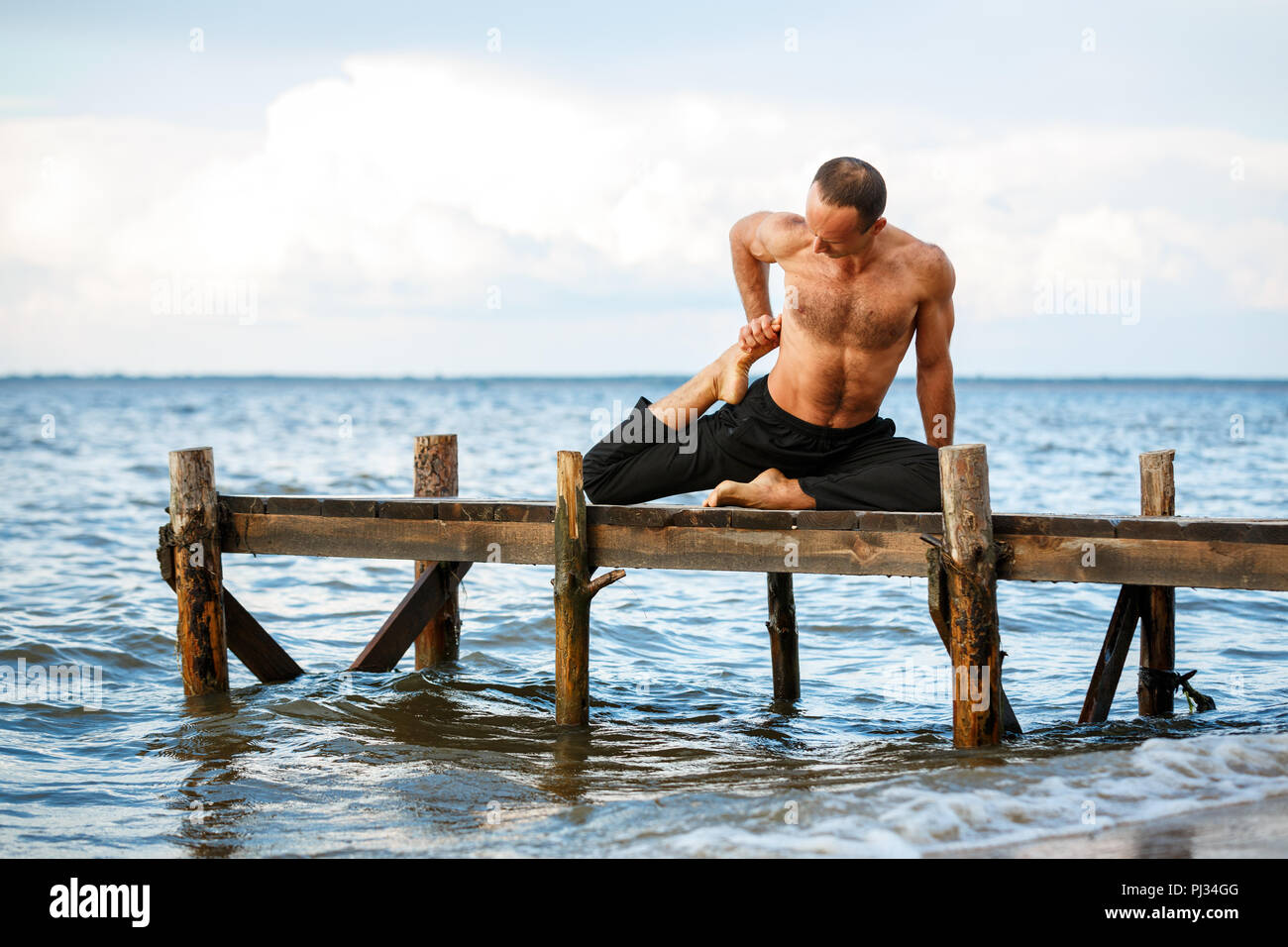 Giovani trainer di yoga pratica di esercizi yoga su un molo in legno su un mare o riva del fiume. Uno stile di vita sano concetto Foto Stock