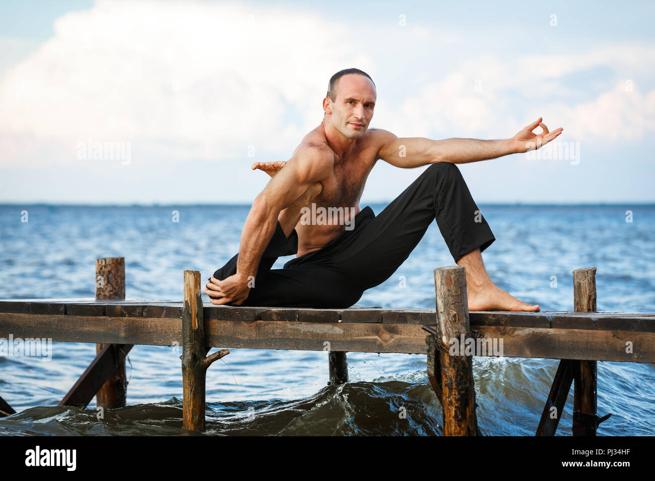 Giovani trainer di yoga pratica di esercizi yoga su un molo in legno su un mare o riva del fiume. Uno stile di vita sano concetto Foto Stock