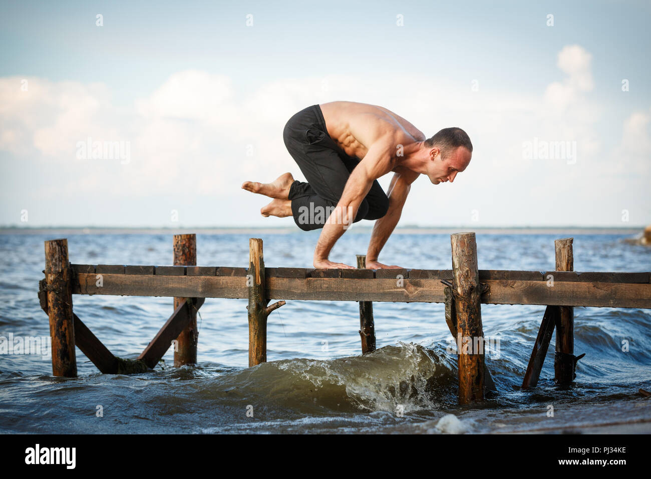 Giovani trainer di yoga pratica lolasana pongono su un molo in legno su un mare o riva del fiume. Uno stile di vita sano concetto Foto Stock