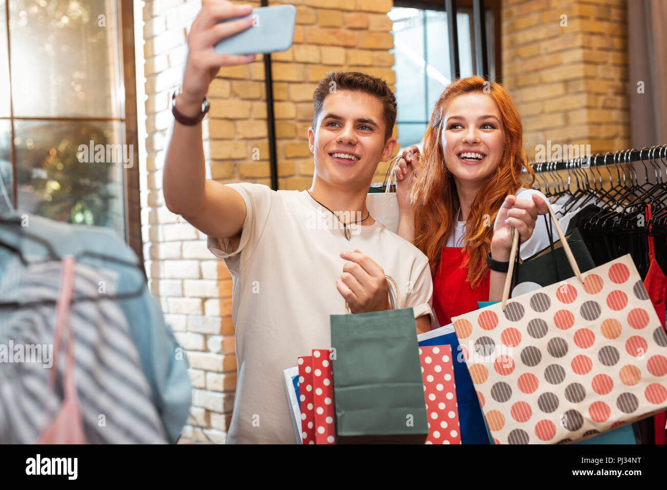 Coppia felice holding di sacchetti di carta e tenendo selfies nel negozio Foto Stock
