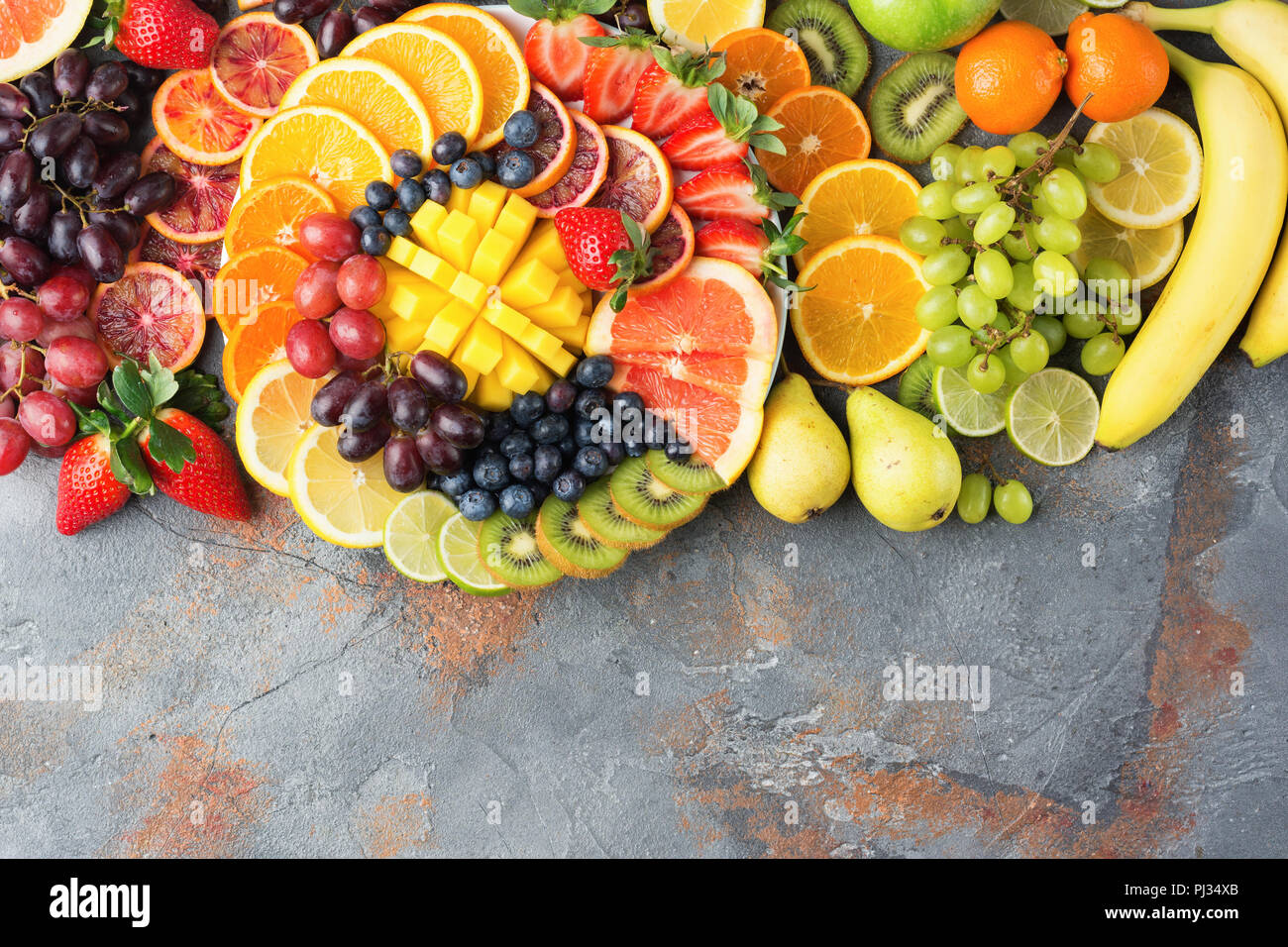 Sani frutti sfondo in colori Arcobaleno arance mele pere uva mango fragole kiwi sul grigio cemento marrone tabella, vista dall'alto, copia di spazio, il fuoco selettivo Foto Stock