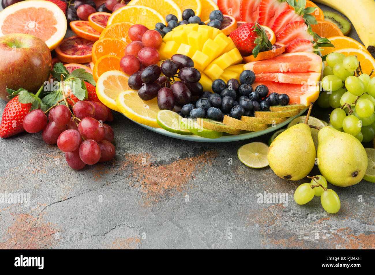 Sani frutti sfondo in colori Arcobaleno arance mele pere uva mango fragole kiwi sul cemento grigio tabella, copia di spazio, il fuoco selettivo Foto Stock