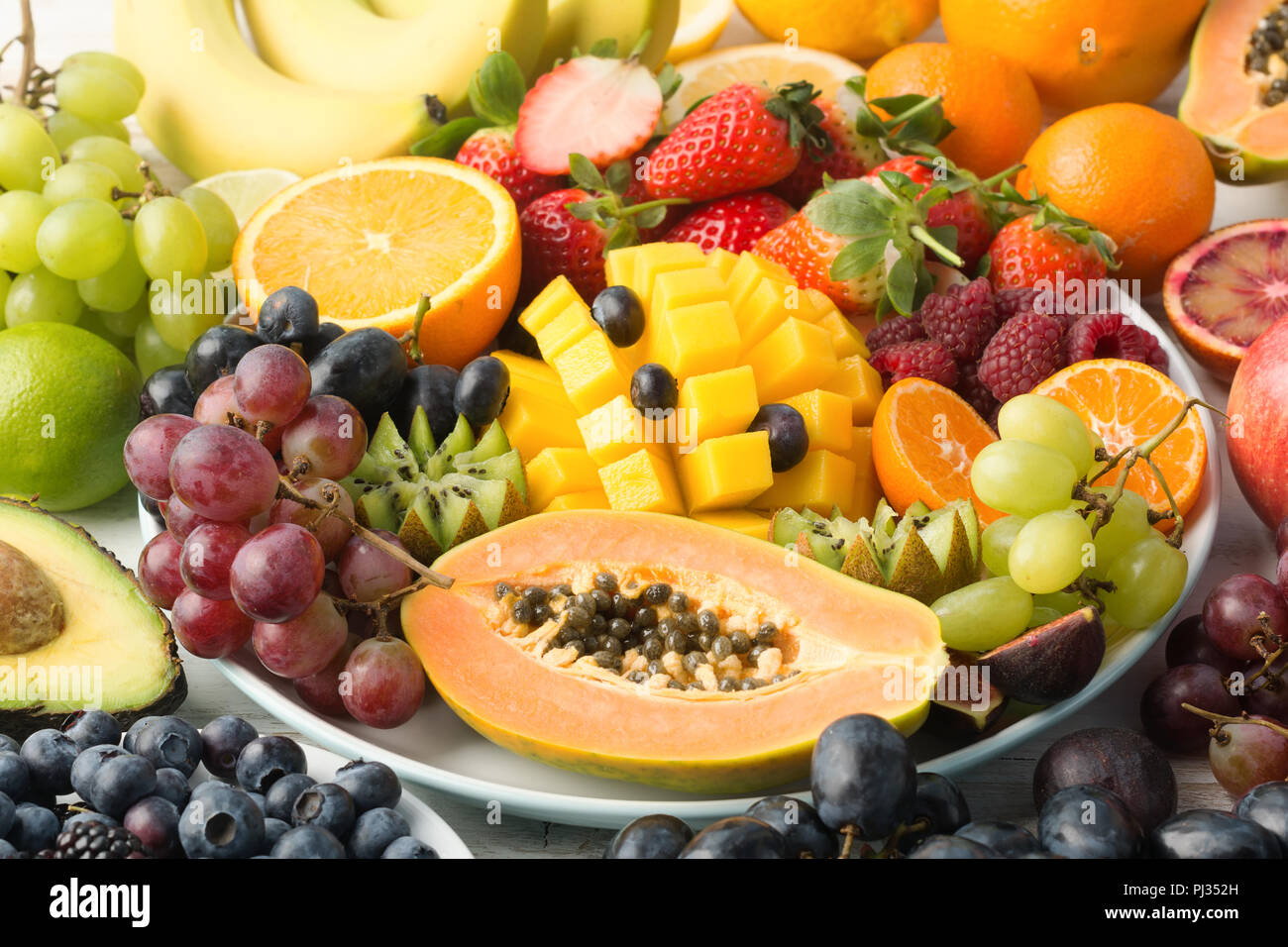 Mangiare sano, di frutta e verdura crude in arcobaleno di colori su una piastra, papaia, mango, uva e bacche, arancio, su off tavolo bianco, il fuoco selettivo Foto Stock