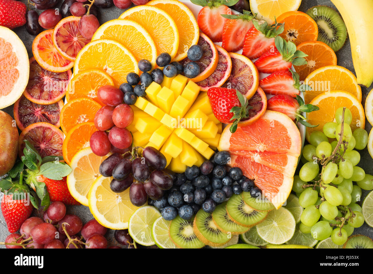 Sani frutti sfondo in colori Arcobaleno arance mele pere uva mango fragole kiwi sul cemento grigio tabella, vista dall'alto, il fuoco selettivo Foto Stock