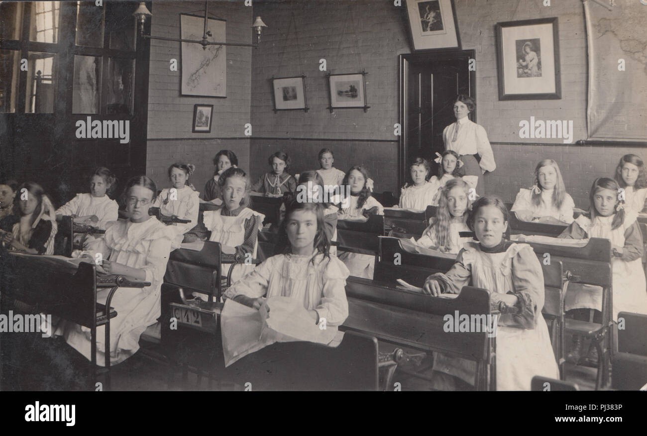 Vintage fotografia di un Edwardian British aula scolastica piena di studentesse. Maestro si fermò sul retro della classe. Foto Stock