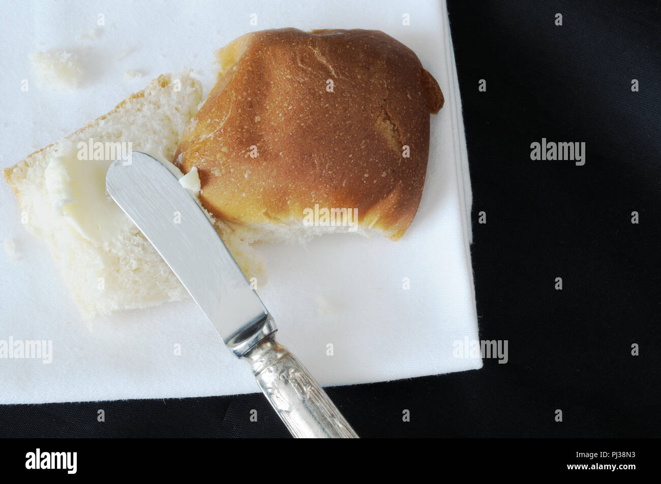 Vista dall'alto di un ricciolo di burro spalmato su un panino, su sfondo nero Foto Stock