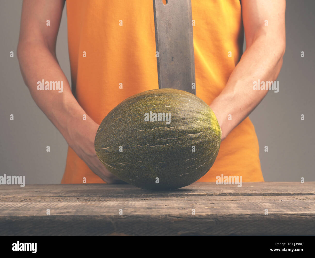 Giovane con un vecchio cleaver e un melone fresco su un rustico tavolo da cucina Foto Stock