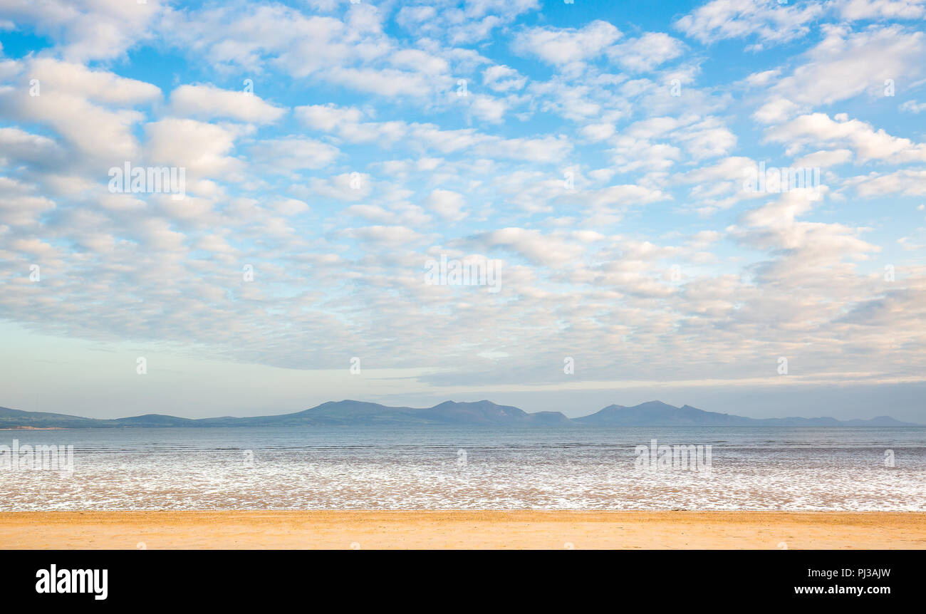 Vista di Yr Eifl montagne da vuoto UK spiaggia sabbiosa Ynys Llanddwyn (isola di marea, Anglesey, Galles). Spettacolari blue sky & wispy, cumulus nubi. Foto Stock