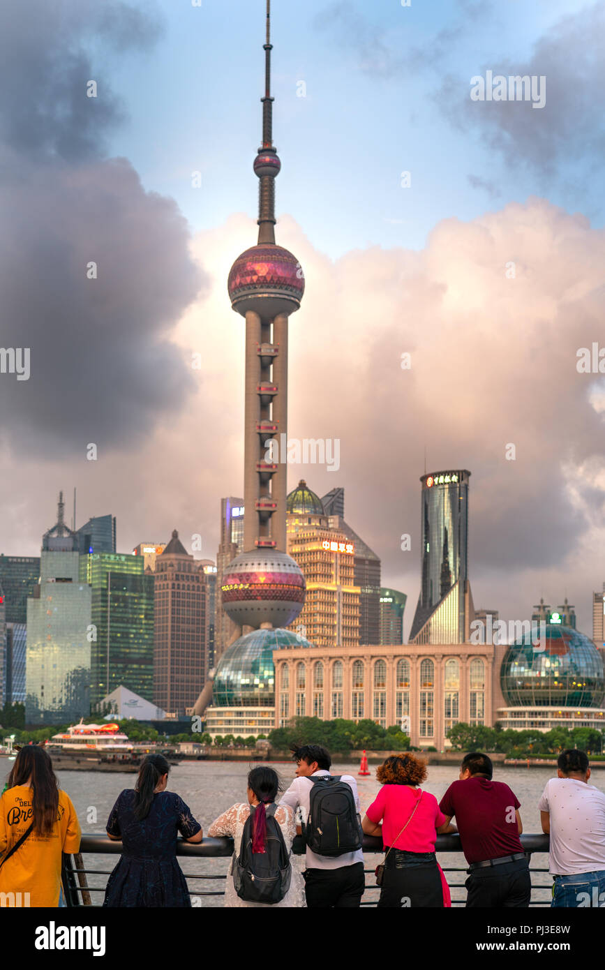 Un gruppo di turisti cinesi appoggiano sulla ringhiera del Bund a Shanghai in Cina e di guardare al di là del fiume di Pudong skyline al tramonto. Foto Stock