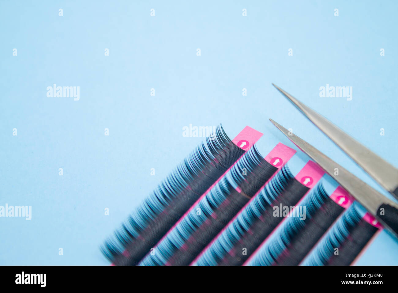 Bellezza e moda concetto - strumenti per extension delle ciglia procedura. Due pinzette con artificiale ciglia nere su sfondo blu. copyspace mockup Foto Stock