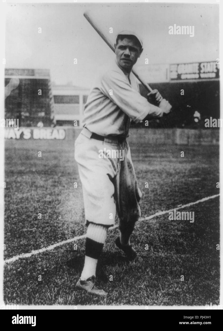 Babe Ruth, ritratto a figura intera, in piedi, rivolto verso la parte anteriore, mantenendo la bat, in baseball uniforme, su campo Foto Stock