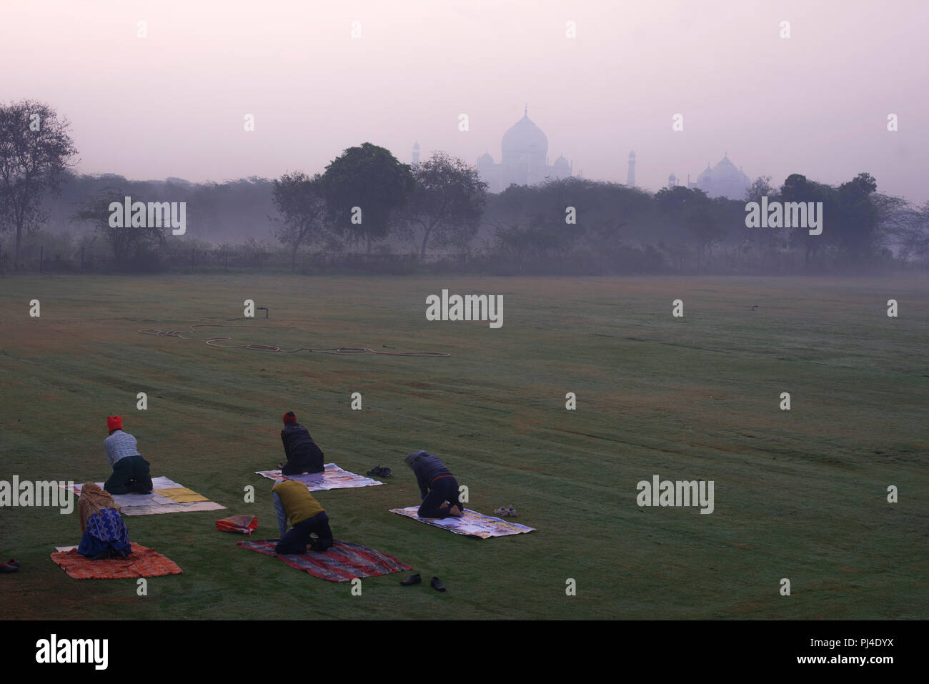 Taj Mahal la meraviglia del mondo e l'orgoglio di India in inverno la luce del mattino e haze con cinque persone facendo yoga in un giardino in primo piano Foto Stock