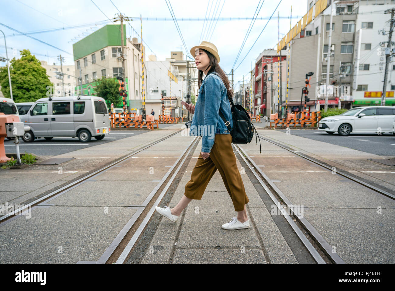 Viaggiare rilassati Donna che cammina attraverso la ferrovia tenendo il suo telefono nella città di Osaka in Giappone. Foto Stock