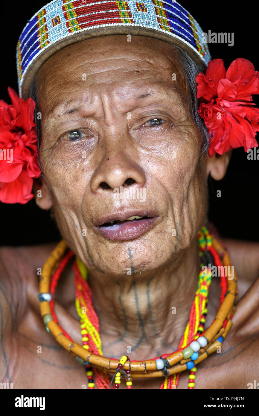 Ritratto di vecchio sciamano di Mentawai persone che indossano fiori rossi sulla sua testa e tatuaggi, tribù indigene, Siberut, Sumatra, Indonesia Foto Stock