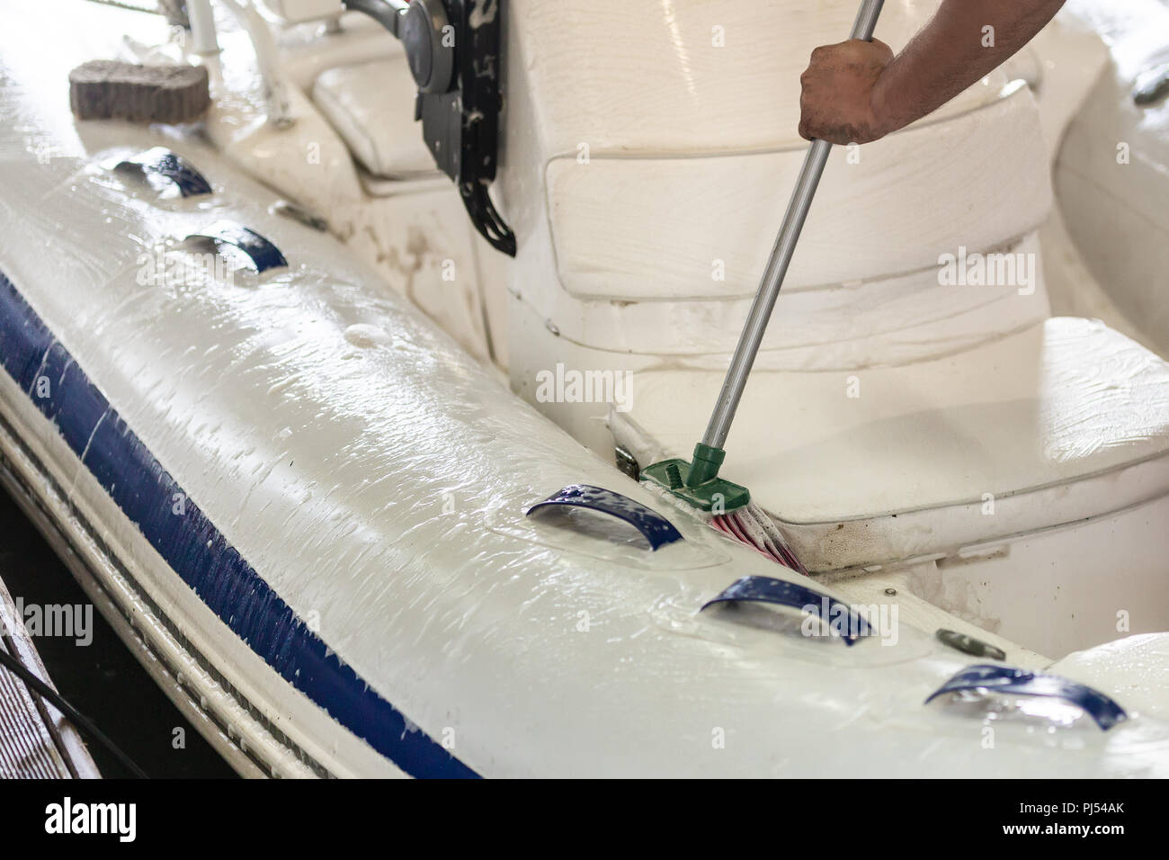 L'uomo bianco lavaggio barca gonfiabile con pennello e con acqua in pressione sistema a garage. Servizio nave e stagionali e un concetto di manutenzione. Foto Stock
