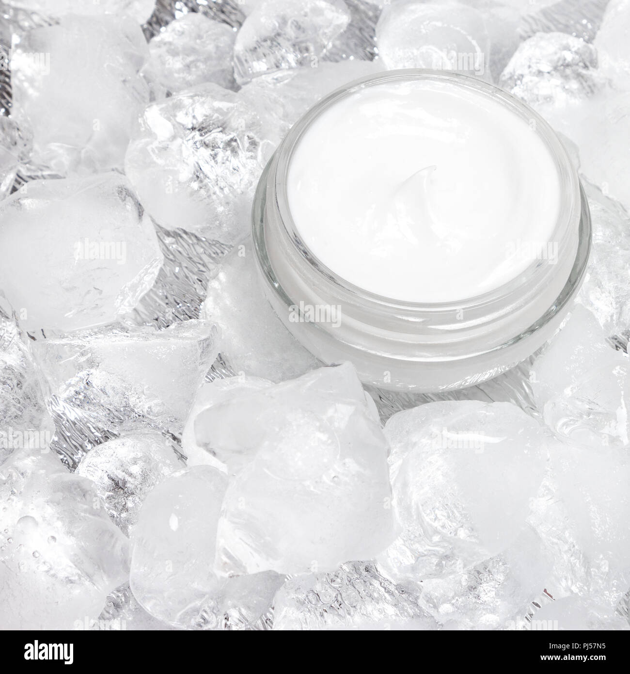 Close-up di aprire il vasetto di vetro con crema circondato da cubetti di ghiaccio. Effetto di raffreddamento prodotto per la cura della pelle Foto Stock