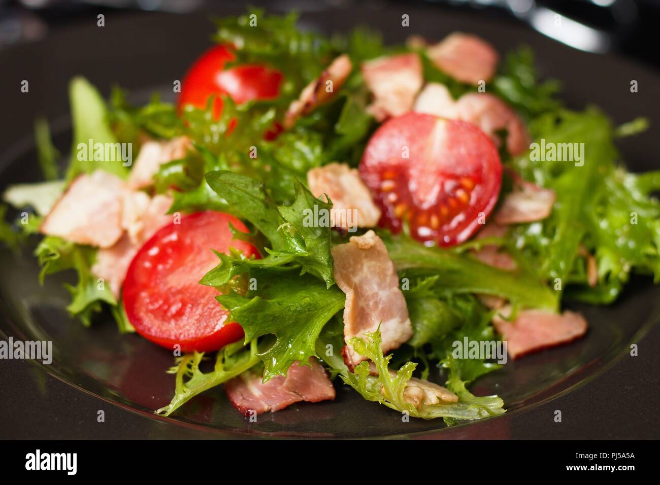 Close up su insalata verde con rossi pomodori ciliegini e strisce di prosciutto Foto Stock