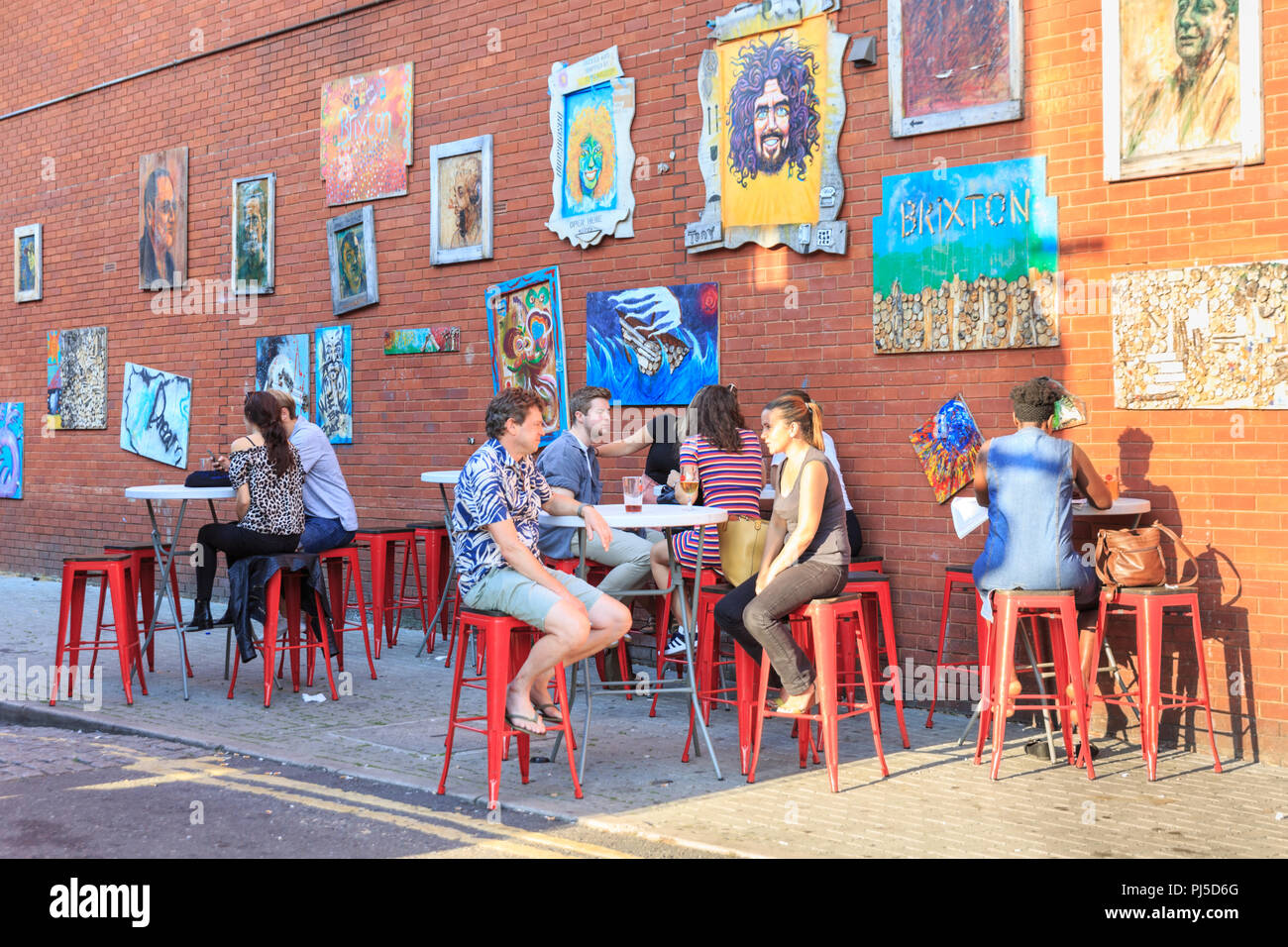 Persone sedersi in strada ritratti arte giardino, una comunità cafe e spazio d'arte in Beehive Place, Brixton, South London, Regno Unito Foto Stock