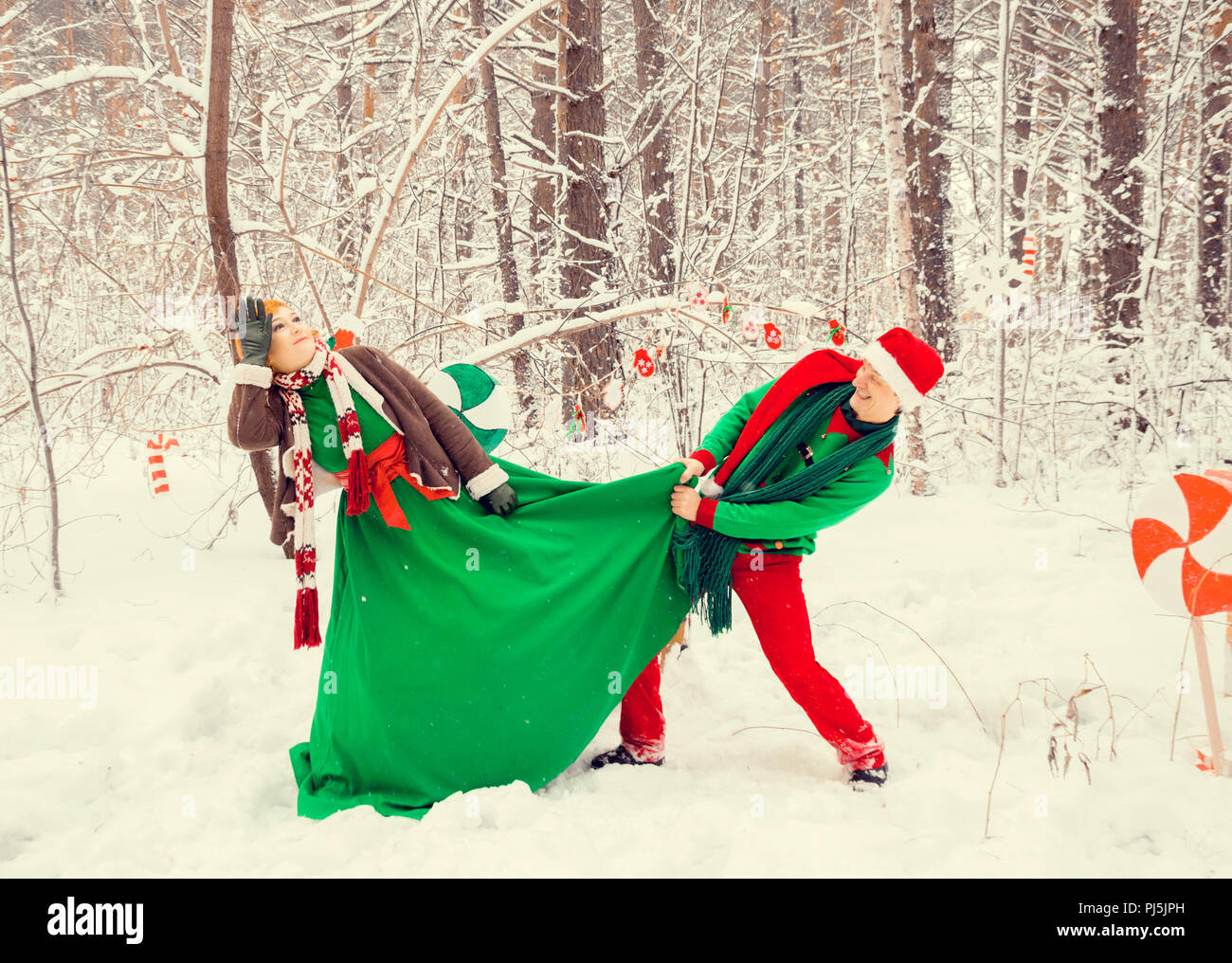 Coppia giovane, il marito e la moglie sono a piedi in costume di fiori tipici degli elfi di Babbo Natale aiutanti in una foresta invernale sotto la neve con un livello di che Foto Stock