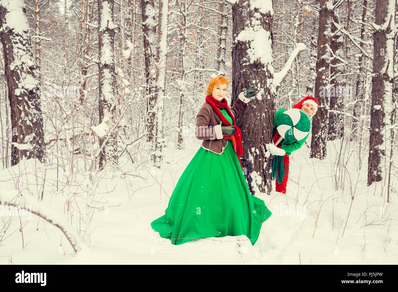 Coppia giovane, il marito e la moglie sono a piedi in costume di fiori tipici degli elfi di Babbo Natale aiutanti in una foresta invernale sotto la neve con un livello di che Foto Stock